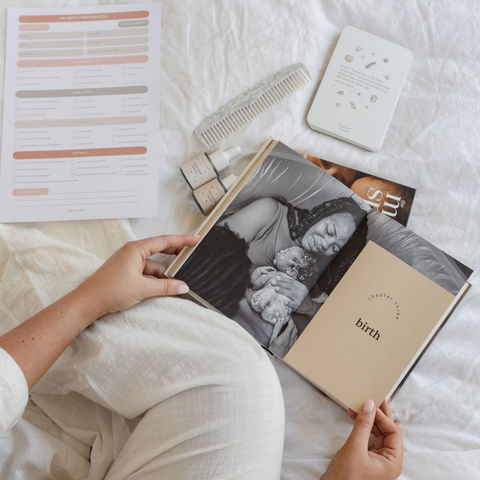 An overview of a mum-to-be sitting on a bed and reading about birth. She is preparing for labour by reading books about birth and books about labour.