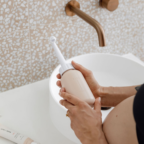 postpartum mother holding perineum wash bottle to use for her recovery.