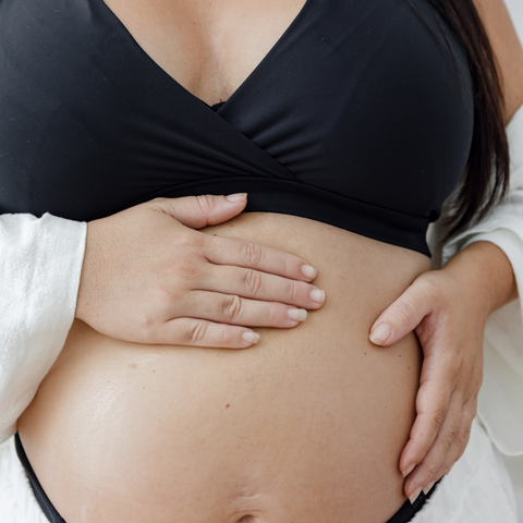 A pregnant woman wearing a maternity bra and maternity briefs stands and holds her belly. She is getting ready to welcome baby to the world.