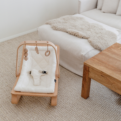 A modern, wooden baby rocker sits on the ground. It’s a great gift for baby play and baby stimulation.