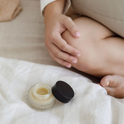 A jar of open nipple cream sits on the bed beside a mother who breastfeeds. It can be used to help cracked or damaged nipples from breastfeeding.