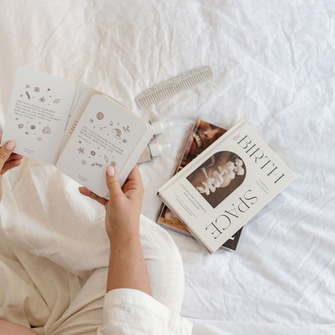 An overview of a mum-to-be with birthing books and preparing for birth. She is reading through birth affirmation cards to mentally prepare for labour.