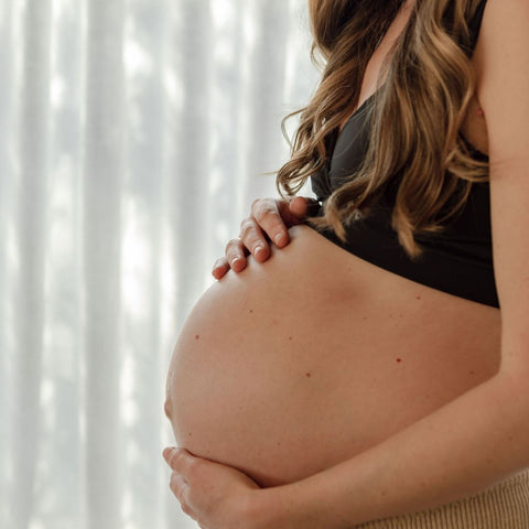 A future mother cradles her pregnancy bump. She looks thoughtful, like she is preparing a birth plan.