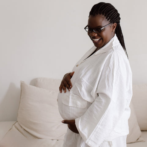 A woman stands side on holding her stomach as she prepares for birth. She is glowing as she is getting ready for birth, labour, and beyond.