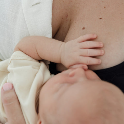 A close up image of the top of a baby’s head as it is cradled to its mother’s breast. The new mum holds her baby tightly after birth as she prepares for postpartum and breastfeeding after birth.