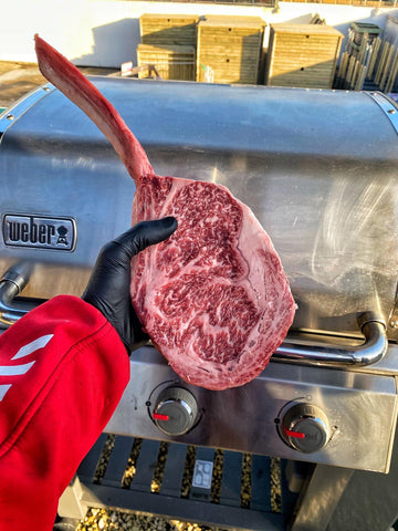 uomo con un taglio di carne in mano e una griglia weber sullo sfondo