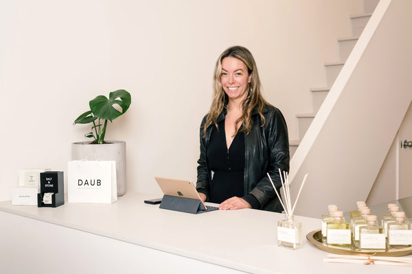 Creative Director and Owner of DAUB, Lexi Soukoreff, stands behind the cash desk smiling at DAUB's first retail location in South Granville.