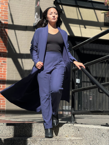 A woman wears a navy blue long jacket and straight leg work pant with a ribbed tank top in black. She's in Yaletown Vancouver and wearing clothing from a local Vancouver brand, DAUB.
