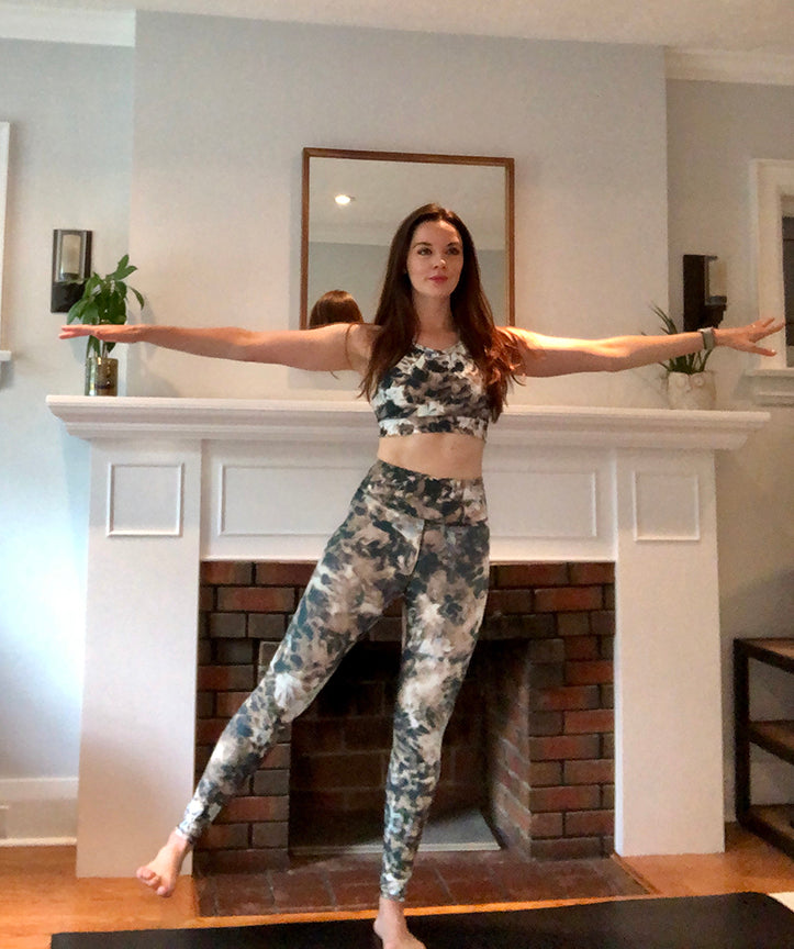 A brunette woman stands and lifts one left to the side to strengthen her hips.