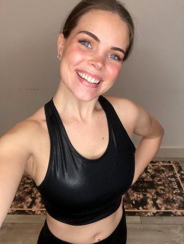 A brunnette woman is seen wearing a black shiny sports bra 