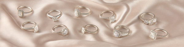 buying an engagement ring | Array of silver diamond rings against a pink silk background.