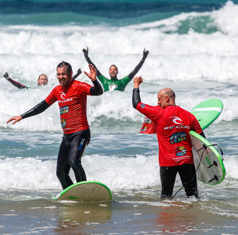 People in the surf with their surfboards – there arms are in the air as they celebrate something