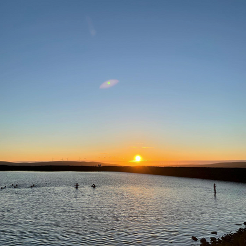 Gaddings Dam at sunset with water in the forefront and small silhouettes of swimmers in the water 