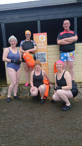 Group of people in their swimming gear next to a sign about the charity swim