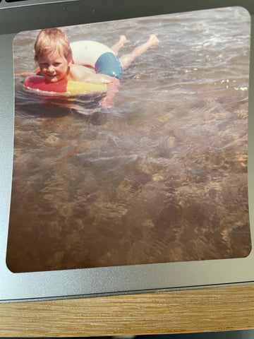 Rachel as a toddler swimming in the sun in a stripey rubber ring