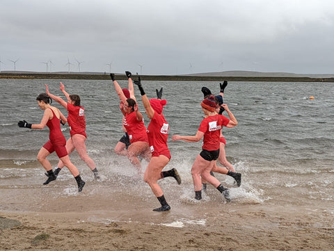 Group of swimmers running into the water wearing red t-shirts all in aid of January Daily Dip 2022