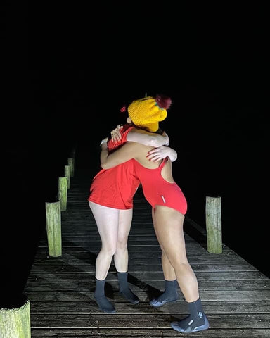 Two people in red swimming costumes hugging in the dark on a pier near the water all in aid of January Daily Dip 2022