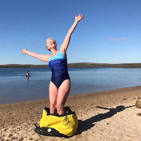 Woman standing in a Swim Feral Turtleback bag with her arms outstretched to the sky, smiling. 