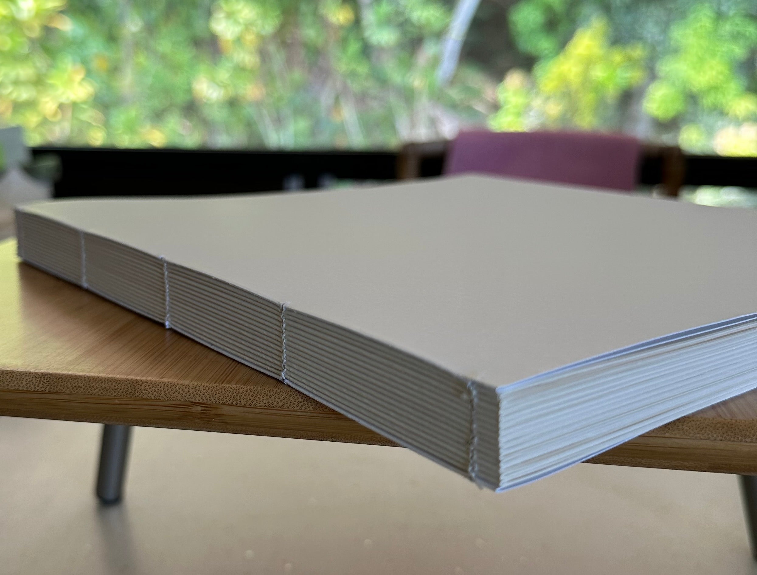 Hand-sewn book text block resting on a wooden workbench, showing exposed binding stitches and stacked paper signatures before the cover is added.