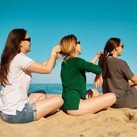 Three women on the beach doing each other's hair.