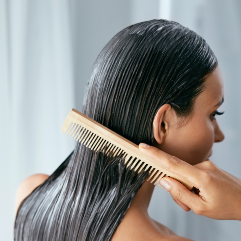 A young woman applying a hair mask with a comb.