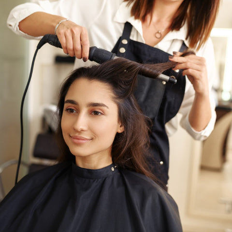 A young woman at a hair salon getting her hair curled with a curling wand.