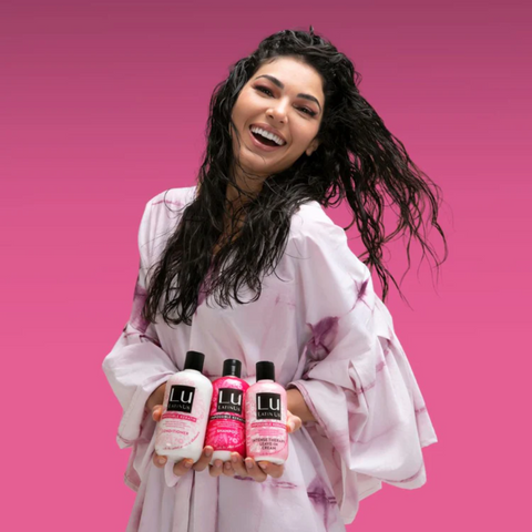 A Latina woman holding a Lu shampoo, conditioner and styling cream from the Lu Rescue Collection.
