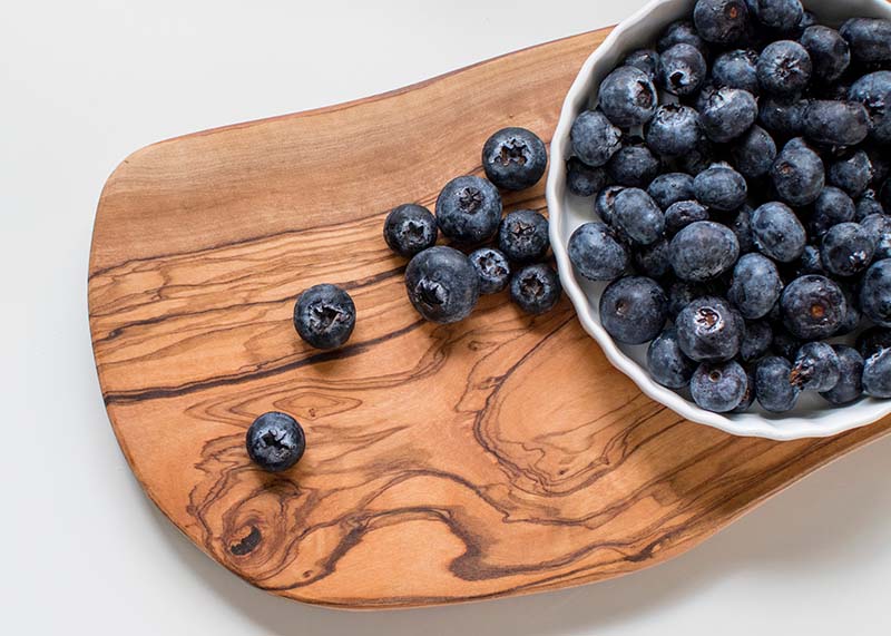 A white bowl of blueberries spilling out onto a wooden cutting board