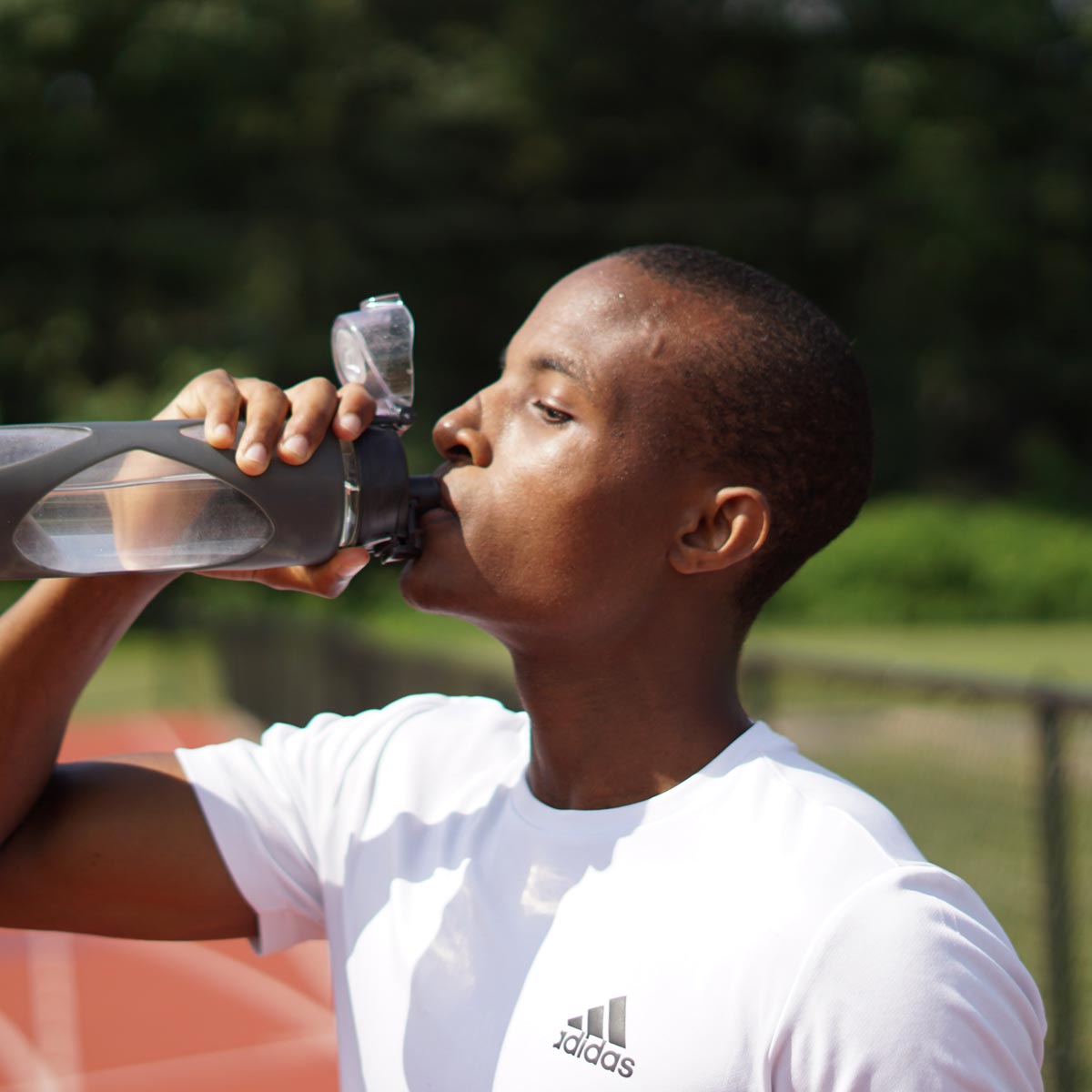 Man drinking from a water bottle at an outdoor running race track