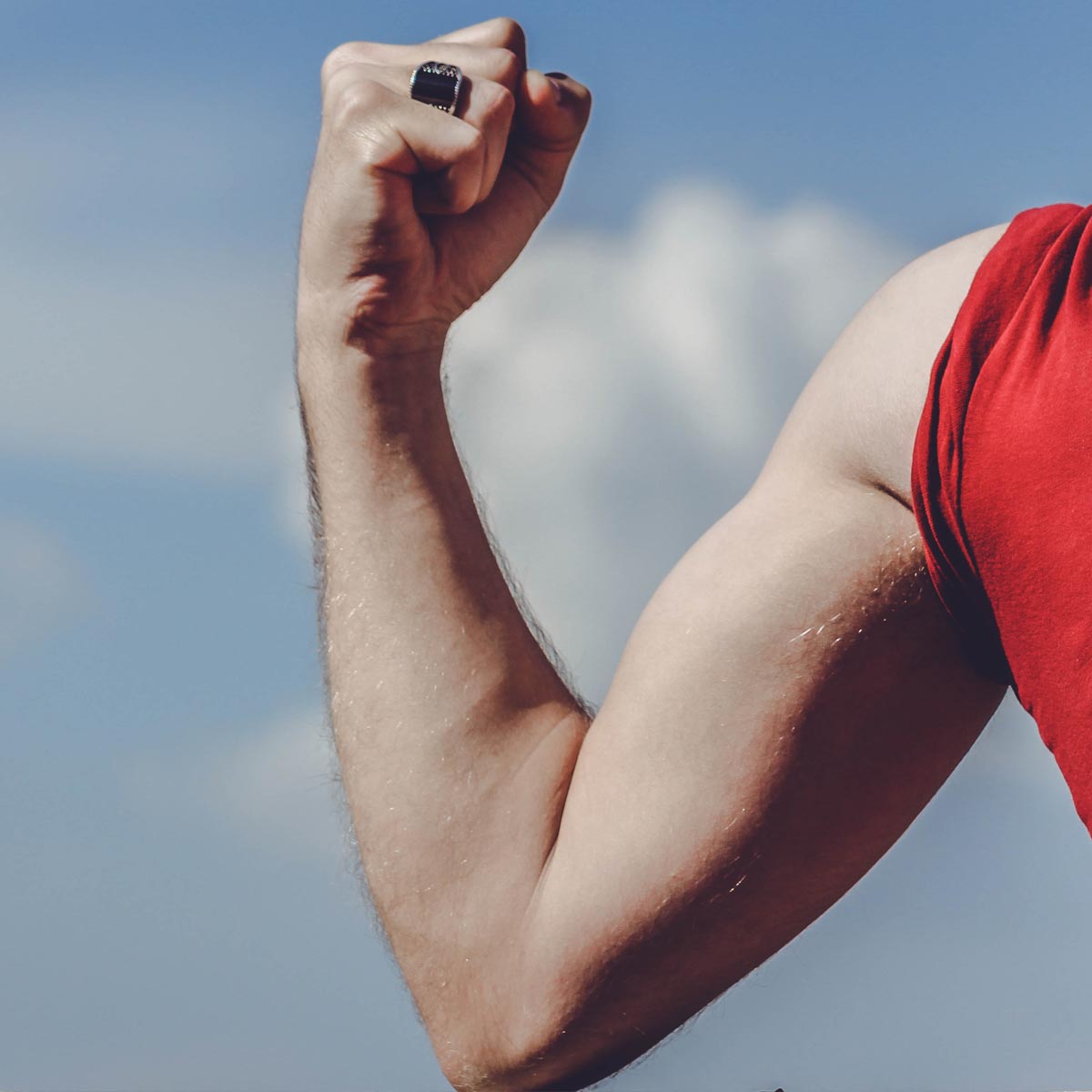 A man in a red t-shirt flexes the muscles on his right arm