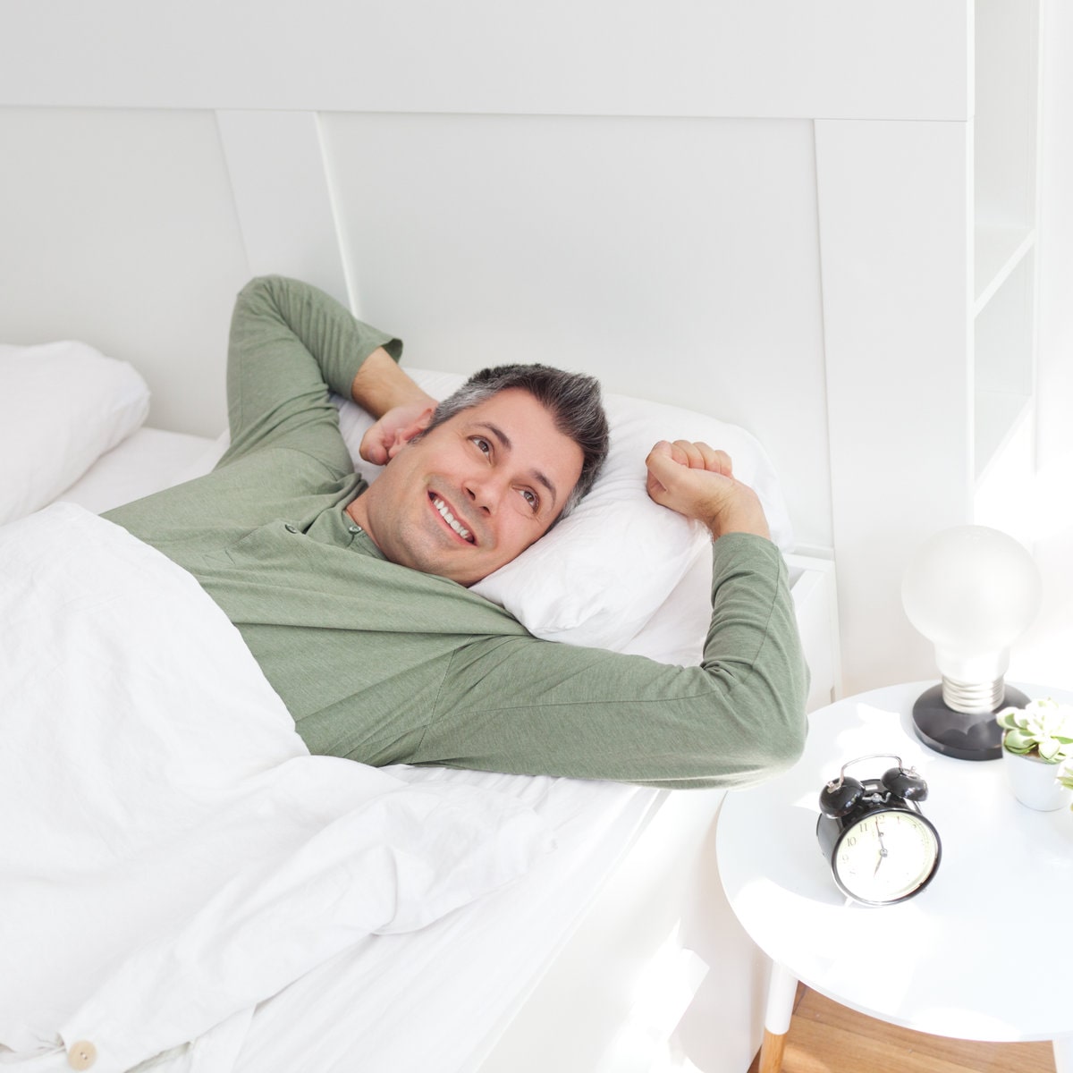 Man wakes up from a nap in a white bed during the daytime and experiences an afternoon energy boost