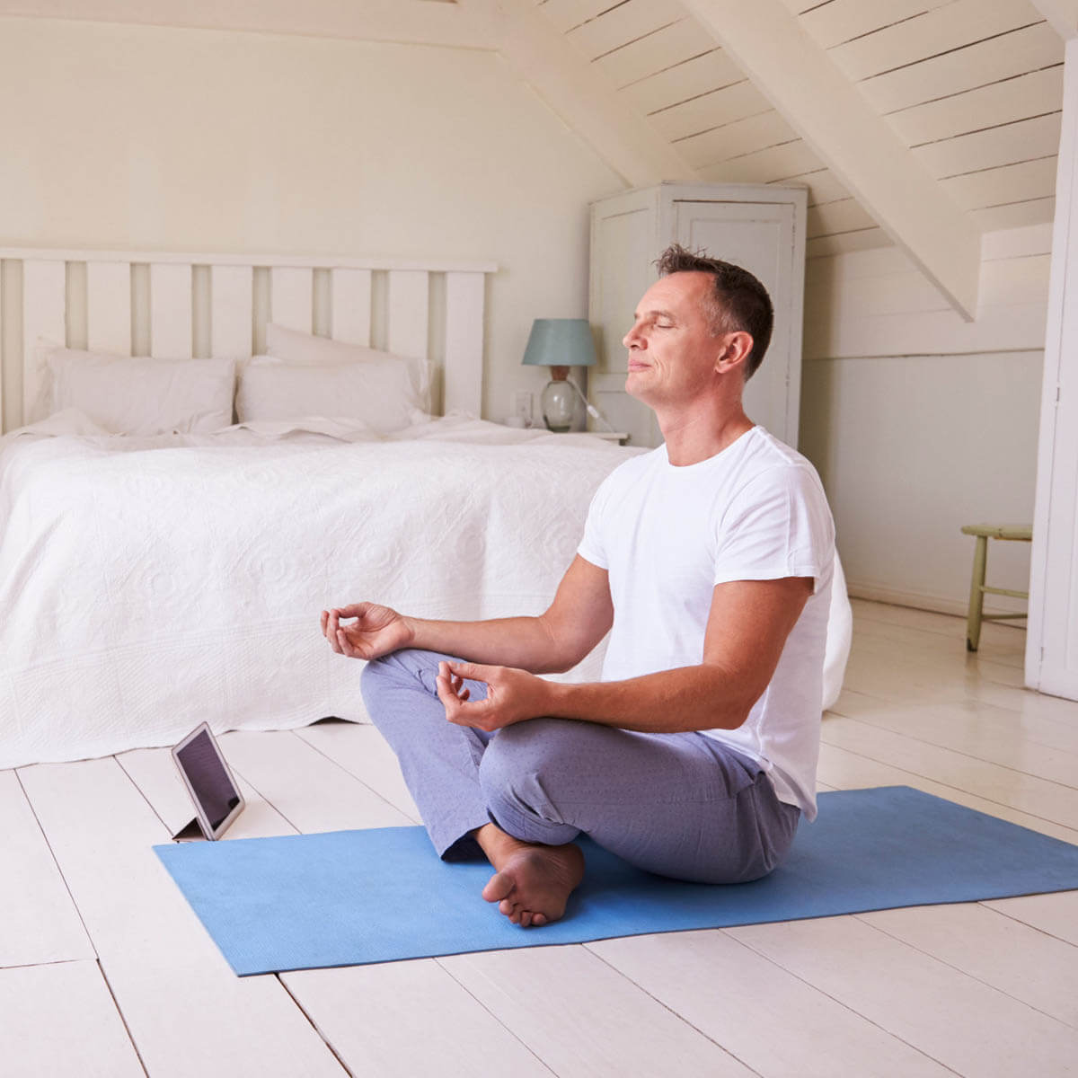 A man uses yoga as a sleep remedy  in his bedroom with a tablet sitting next to him