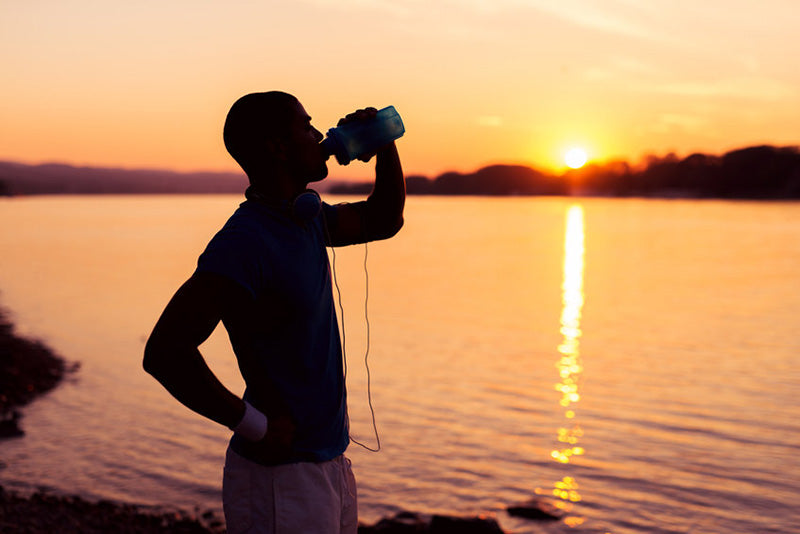 Running hydrating during sunset in front of a lake.