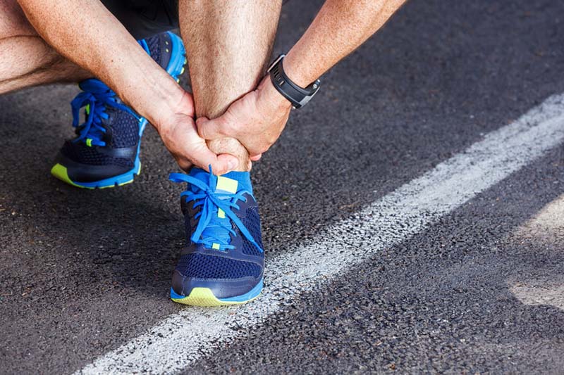 Man in pain, holding his ankle during the middle of a run.