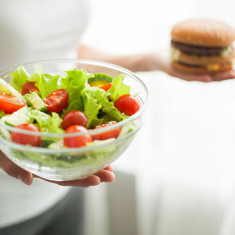 A woman holding a salad in one hand and a burger in the other, trying to outweigh which one is the better option
