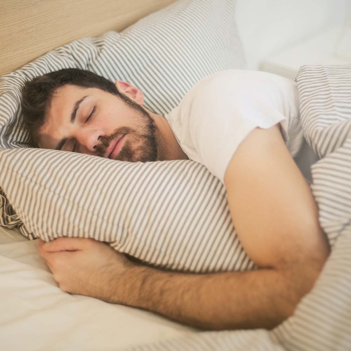 Man in a white T-shirt sleeps in a cozy, soft bed