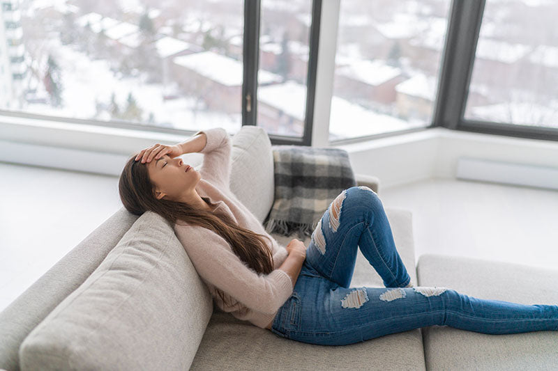 A dehydrated woman sitting on the couch with her hand to her forehead on a wintry day