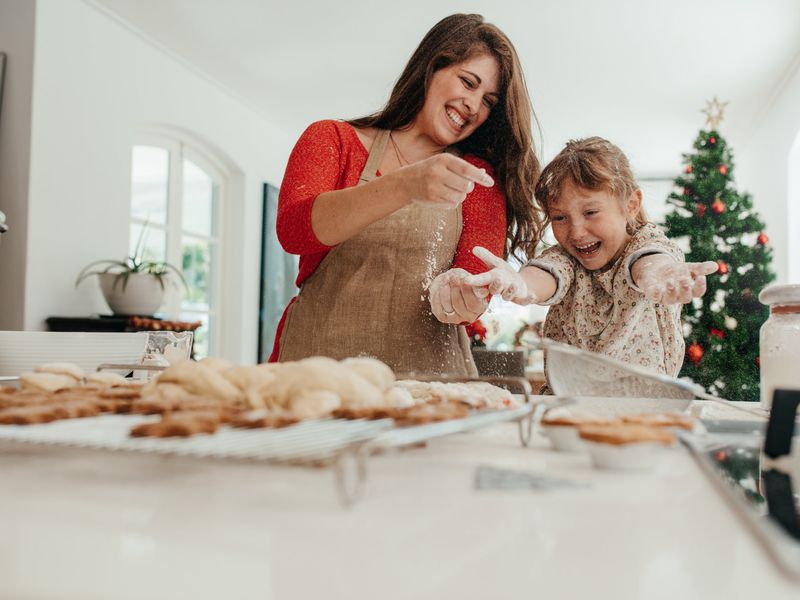 A mother and her daughter laugh as they play with flour and make Christmas cookies