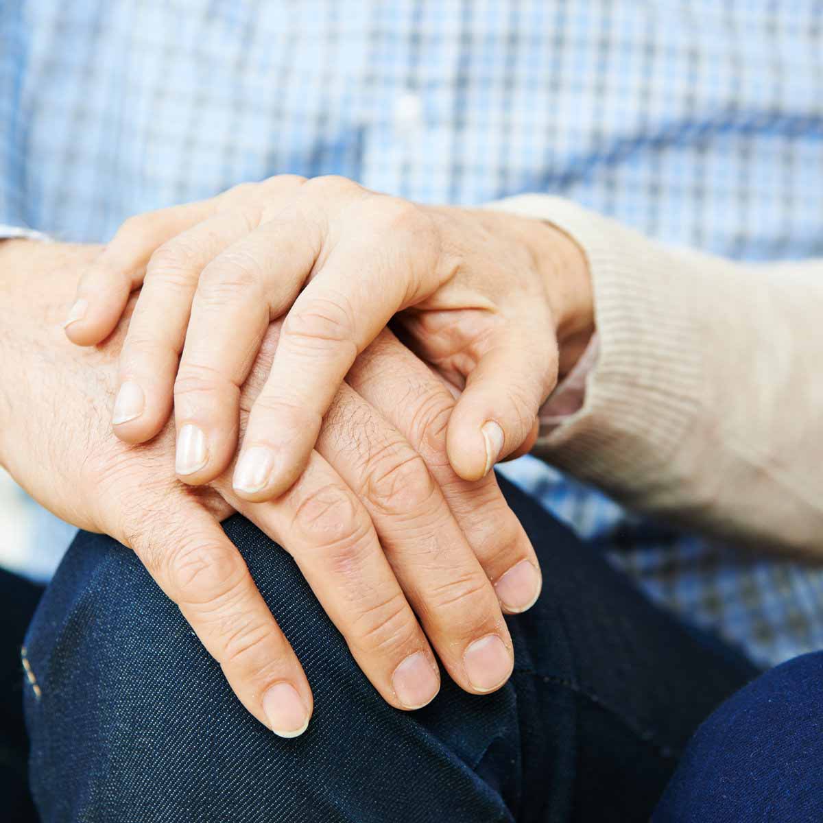 An elderly woman holds the hand of an elderly man to comfort him through a challenge