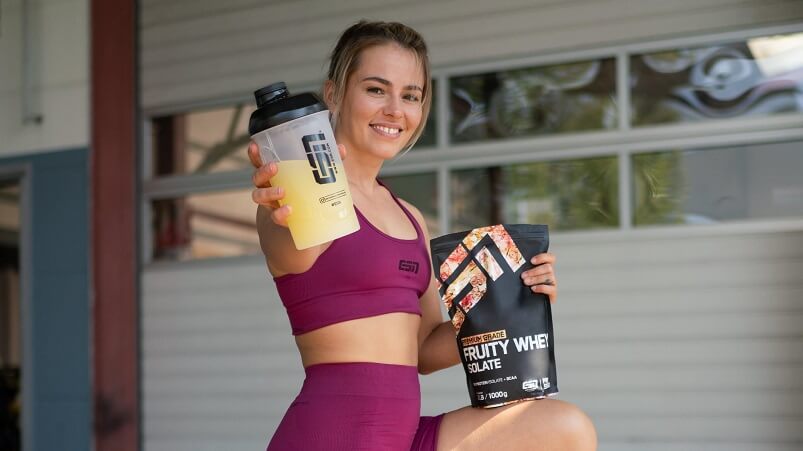 Frau hält Shake mit fruchtigem Whey Isolat von ESN sowie eine Tüte des Fruity Whey Isoalte Pulvers