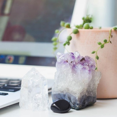 An amethyst cluster, clear quartz, and obsidian stone placed in front of a computer - healing crystals for your office space