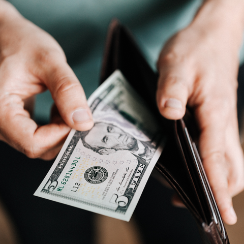 Man opening his wallet and taking a $5 dollar bill - Image from Canva