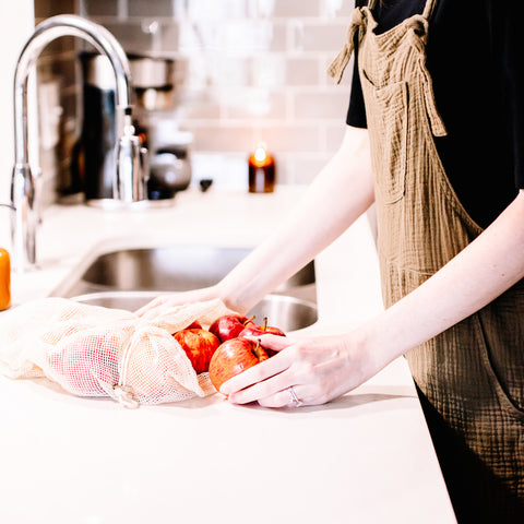 Woman taking apples out of a reusable produce cotton bag in her kitchen