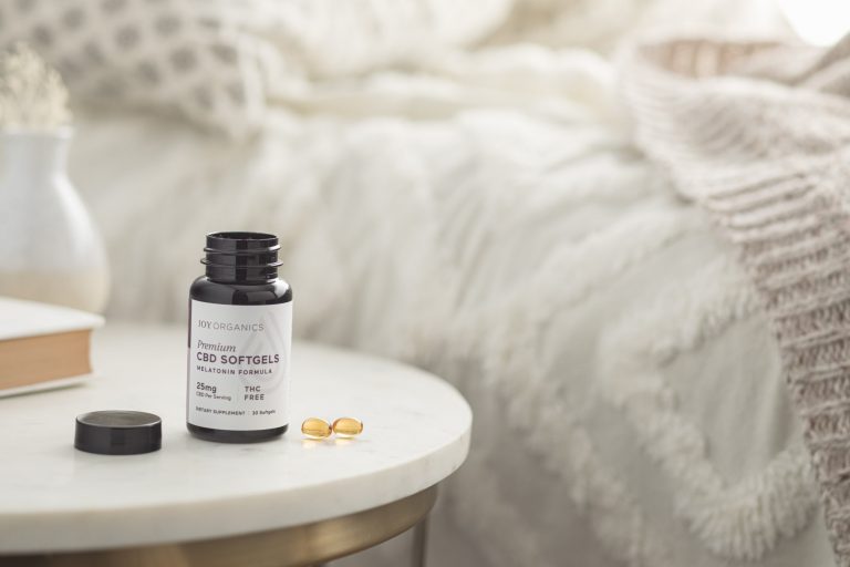 Joy Organics Melatonin CBD Softgels next to a bed