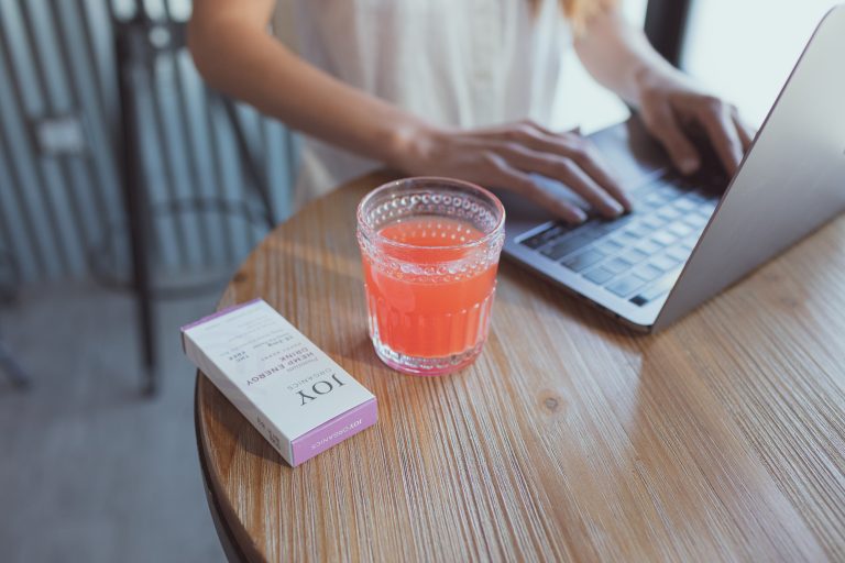 CBD energy drink mix in glass next to woman on laptop