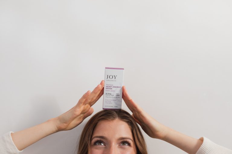 Woman holding Joy Organics CBD Energy Drink Mix box on her head