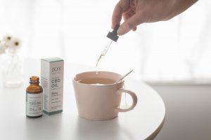 hand dropping Mint CBD Oil into mug of tea