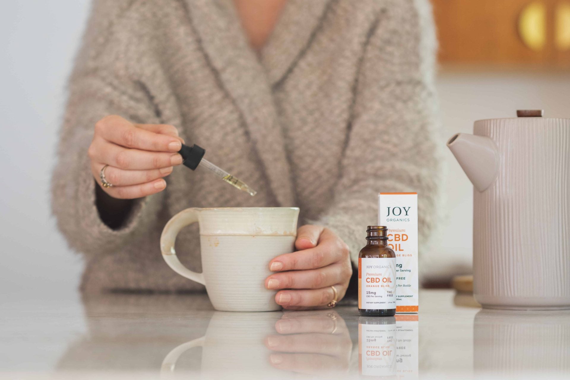 woman dropping orange CBD tincture into mug