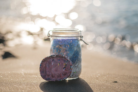 A MamaGaia soap dish leaning against a glass jar, filled with chipped plastic on a beach.