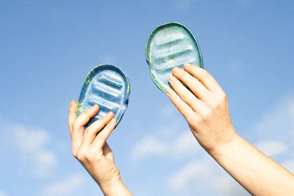 Two hands holding a soap dish each up to the sky, which is blue with some wispy clouds.